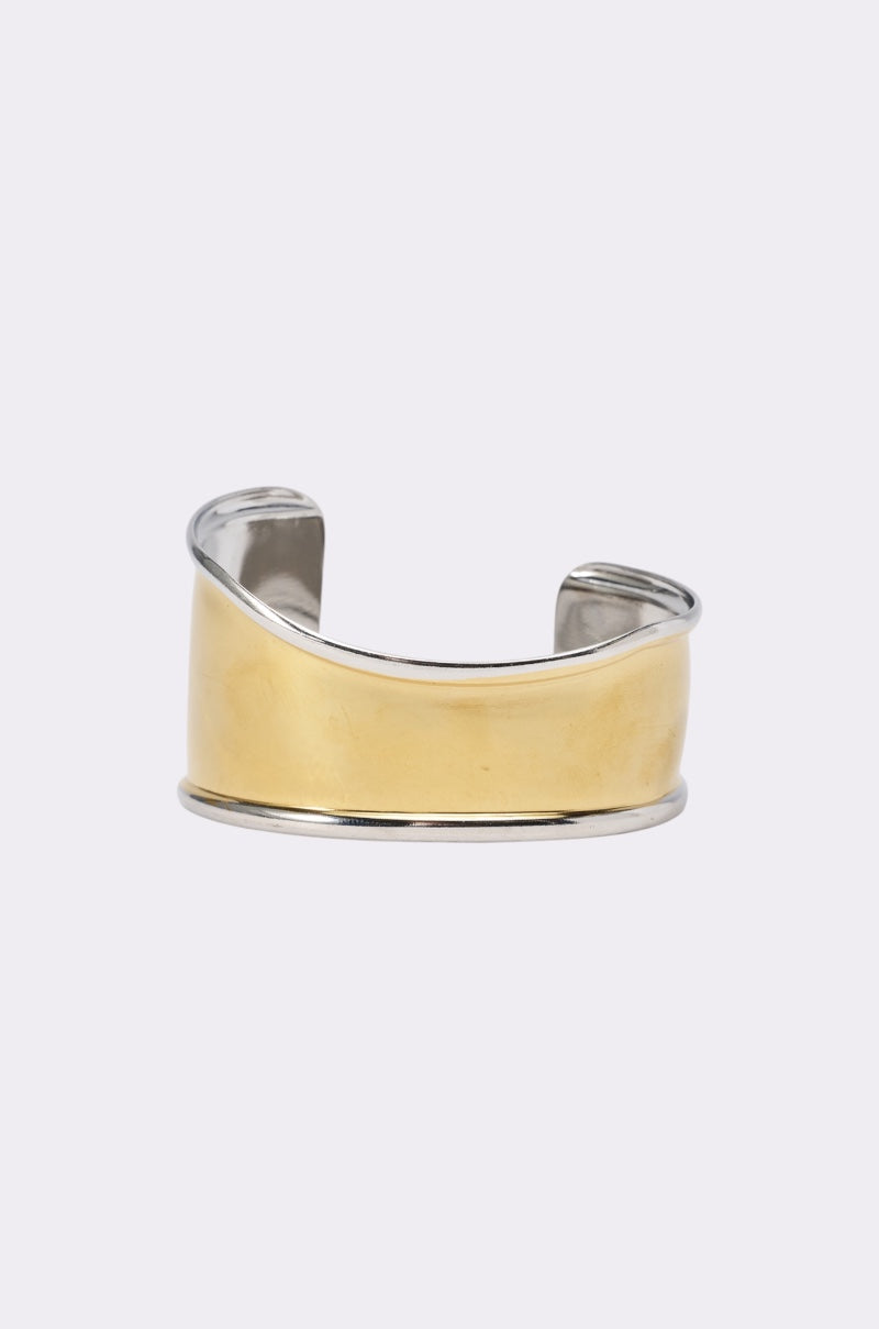 The CUFFING SZN BRACELET is a wide, sculptural cuff with a smooth gold center and silver edges, shown against a plain light background. 0