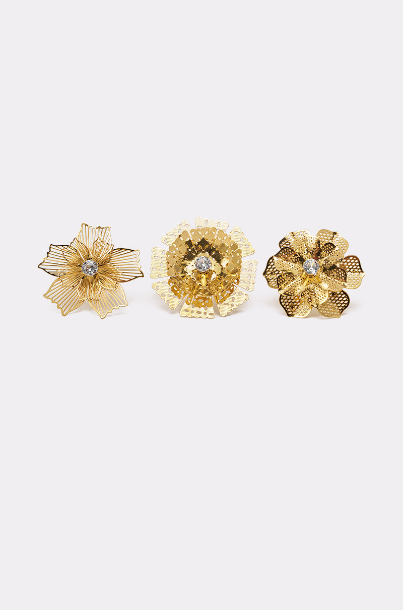 The LETS PARTY RING SET features three gold flower-shaped adjustable rings with intricate designs and central clear gemstones, displayed side by side on a plain white background. 0