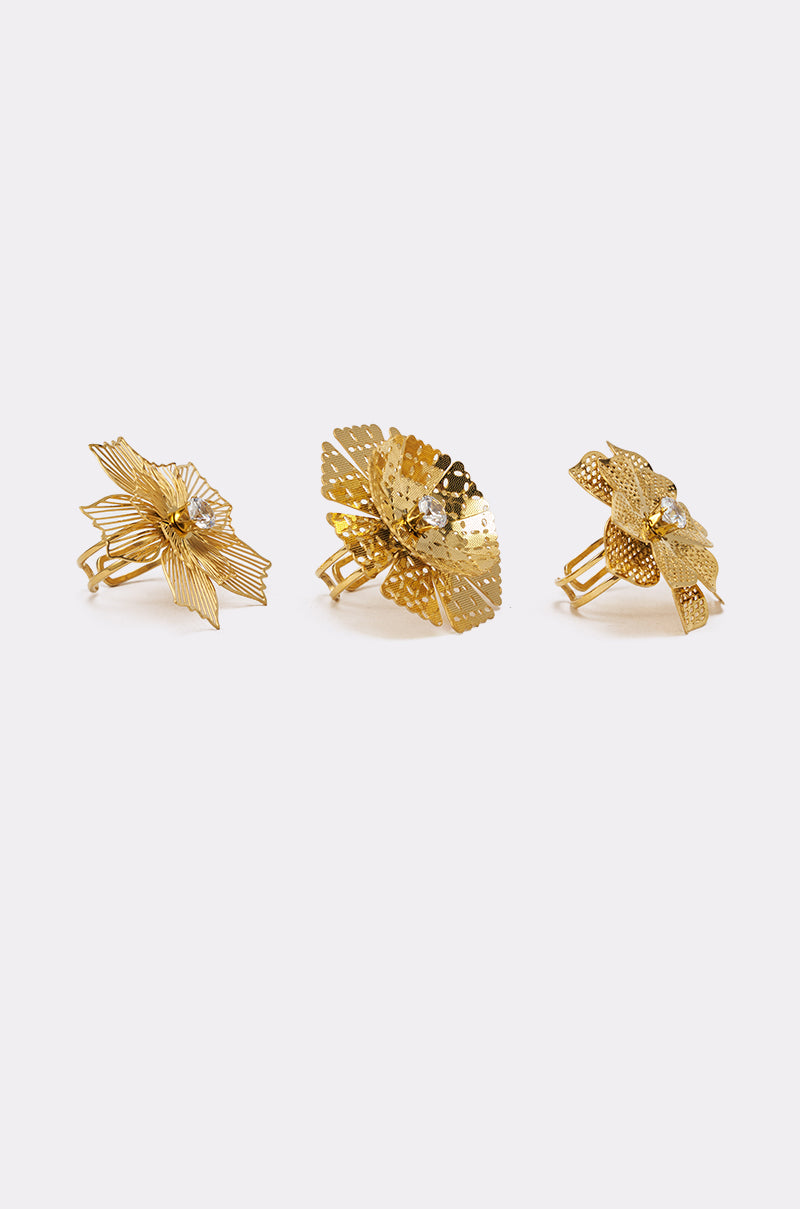 The LETS PARTY RING SET features three elegant gold rings, each with a unique floral design, central accent, and adjustable bands for a perfect fit, beautifully arranged in a row on a plain white background. 2