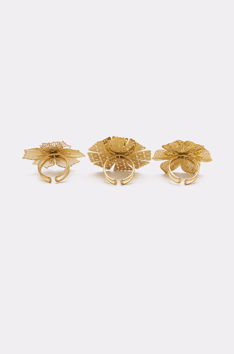 The LETS PARTY RING SET features three adjustable gold rings, each with a unique flower-inspired pattern. Displayed side by side on a white background, the set highlights detailed craftsmanship and intricate floral designs. 3