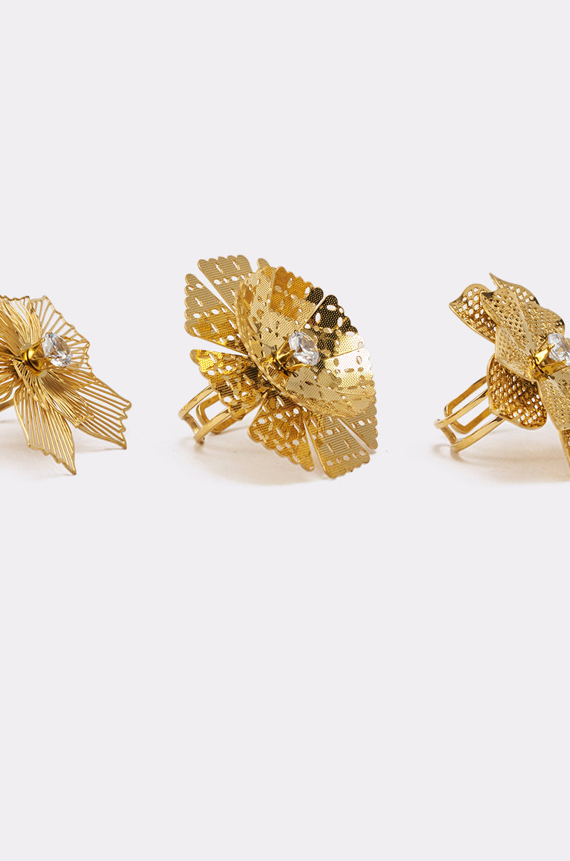 The LETS PARTY RING SET features three gold rings with detailed floral designs and central sparkling stones, arranged side by side on a light background and featuring adjustable bands for a comfortable fit. 4