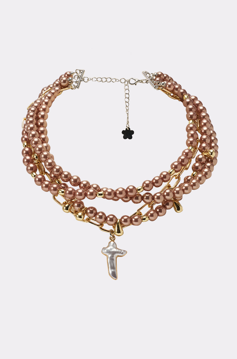 The TAKE IT THERE NECKLACE features three strands of rose gold faux pearls, gold chain links, and a dangling irregular cross pendant. It’s finished with gold accents, a silver clasp, and an adjustable chain for the perfect fit. 0