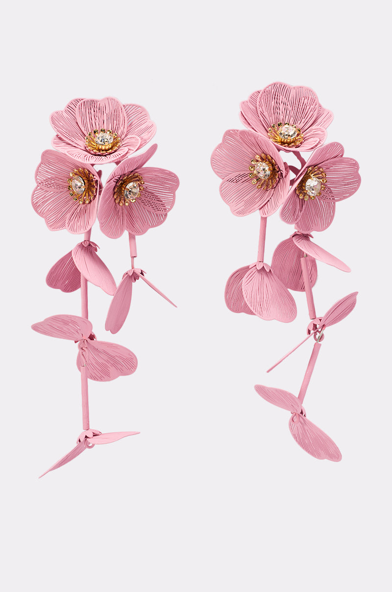 The DO TOO MUCH EARRING features pink flower shapes with layered petals, gold-tone centers, and dangling petal accents, designed to resemble blooming orchids. 2