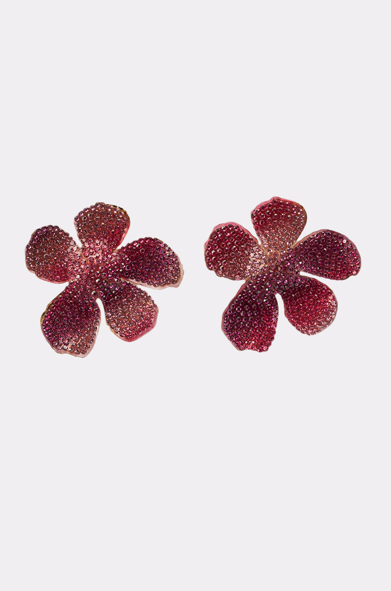 The WORTHY EARRING features two red, five-petaled floral studs with a textured, sparkling surface, displayed on a plain white background. 2