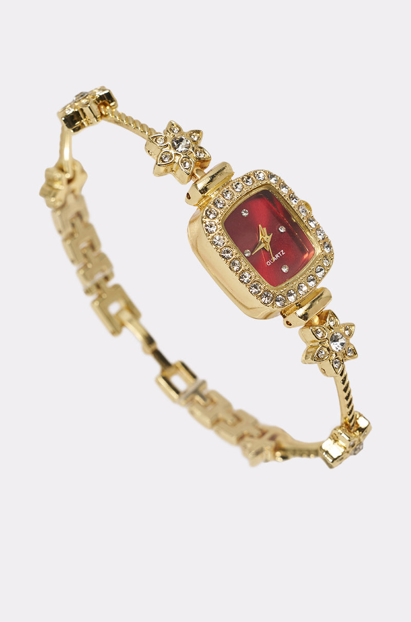 The ELEGANCE WATCH features a gold-tone vintage-inspired design with a red rectangular dial, rhinestone accents framing the face, and flower-shaped decorations on the band, shown against a light background. 0