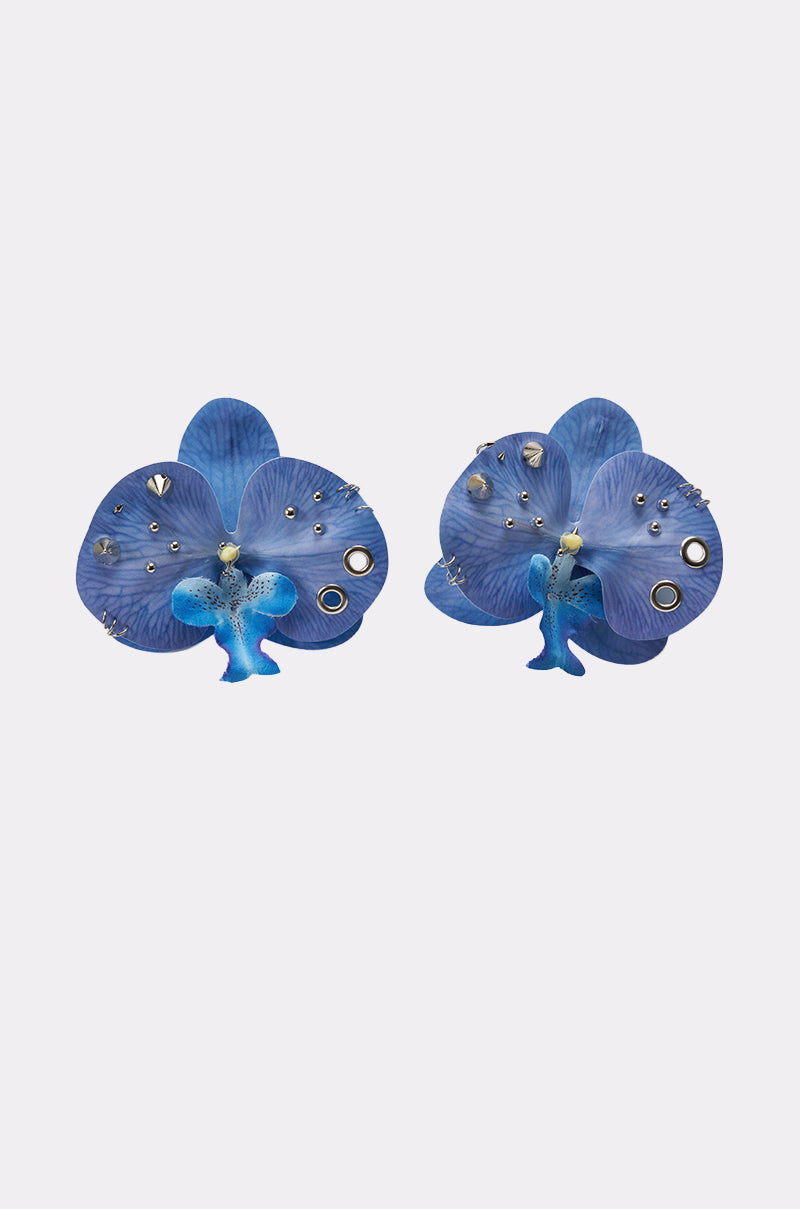 The EDGY VIBES EARRING features cobalt blue orchid petal shapes with delicate flower forms, accented by small silver studs and circular details, all displayed on a light grey background. 1
