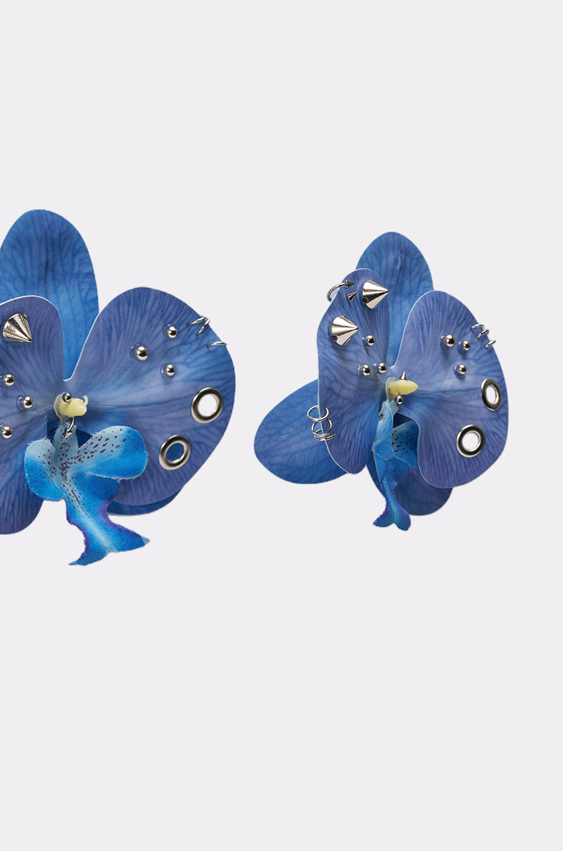 The EDGY VIBES EARRING features two cobalt blue, orchid-shaped statement earrings adorned with silver studs and rings, set against a plain white background. 4