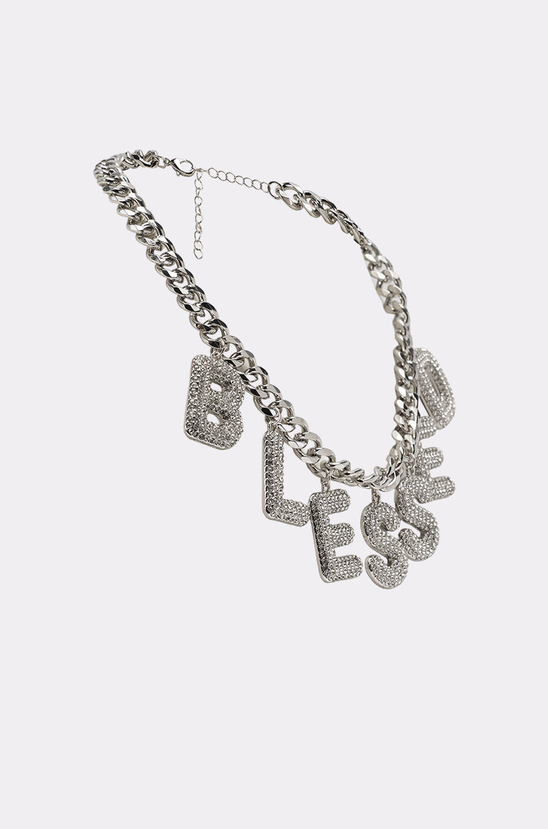 The BEYOND BLESSED NECKLACE is a bold silver chain with large pavé charms spelling "BLESSED," encrusted with rhinestones—the ultimate statement piece shown on a plain white background. 2