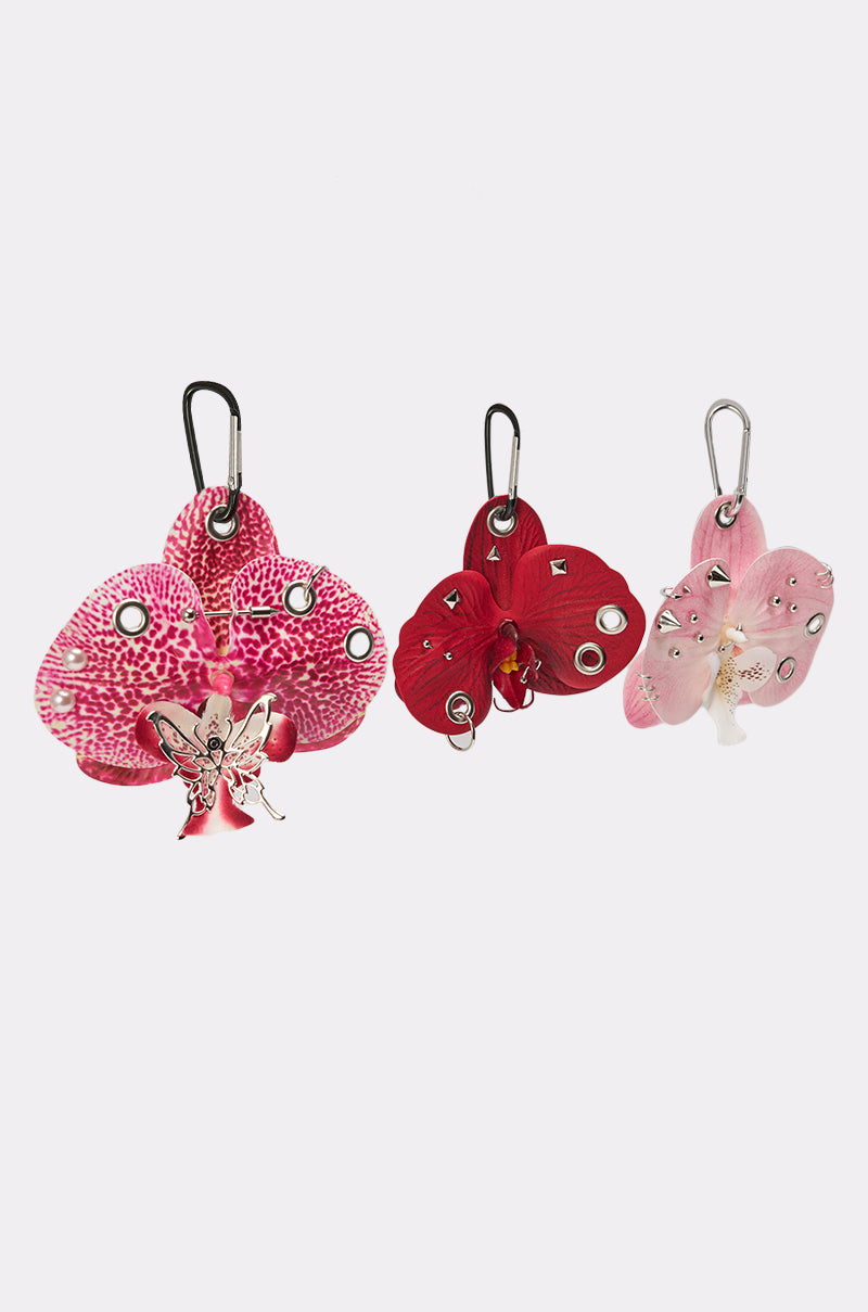 The PIERCED ORCHID FLOWER KEYCHAIN SET features three butterfly-shaped keychains in pink and red, accented with metallic studs, floral charms, and a carabiner clasp for a trendy Y2K look. Displayed on a light background. 3