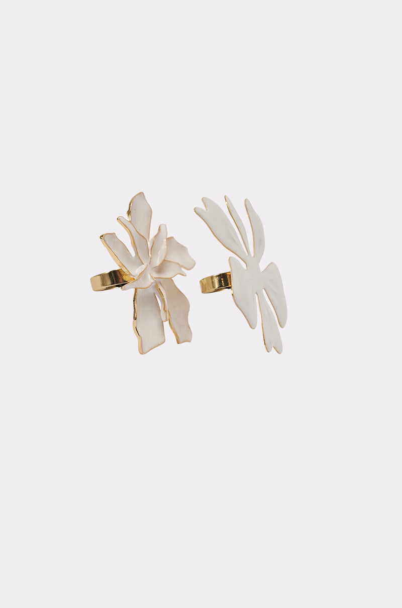 The IN BLOOM RING SET features two gold-trim flower rings with bold white abstract floral designs, beautifully showcased against a simple light background. 1