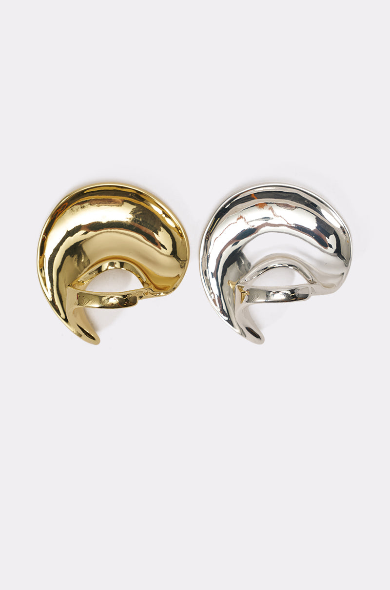 The CROSS MY HEART RING SET features two sculptural, abstract metal rings—one in shiny gold and one in shiny silver—with curved, organic shapes that echo the bold look of chunky jewelry, displayed on a plain white background. 3