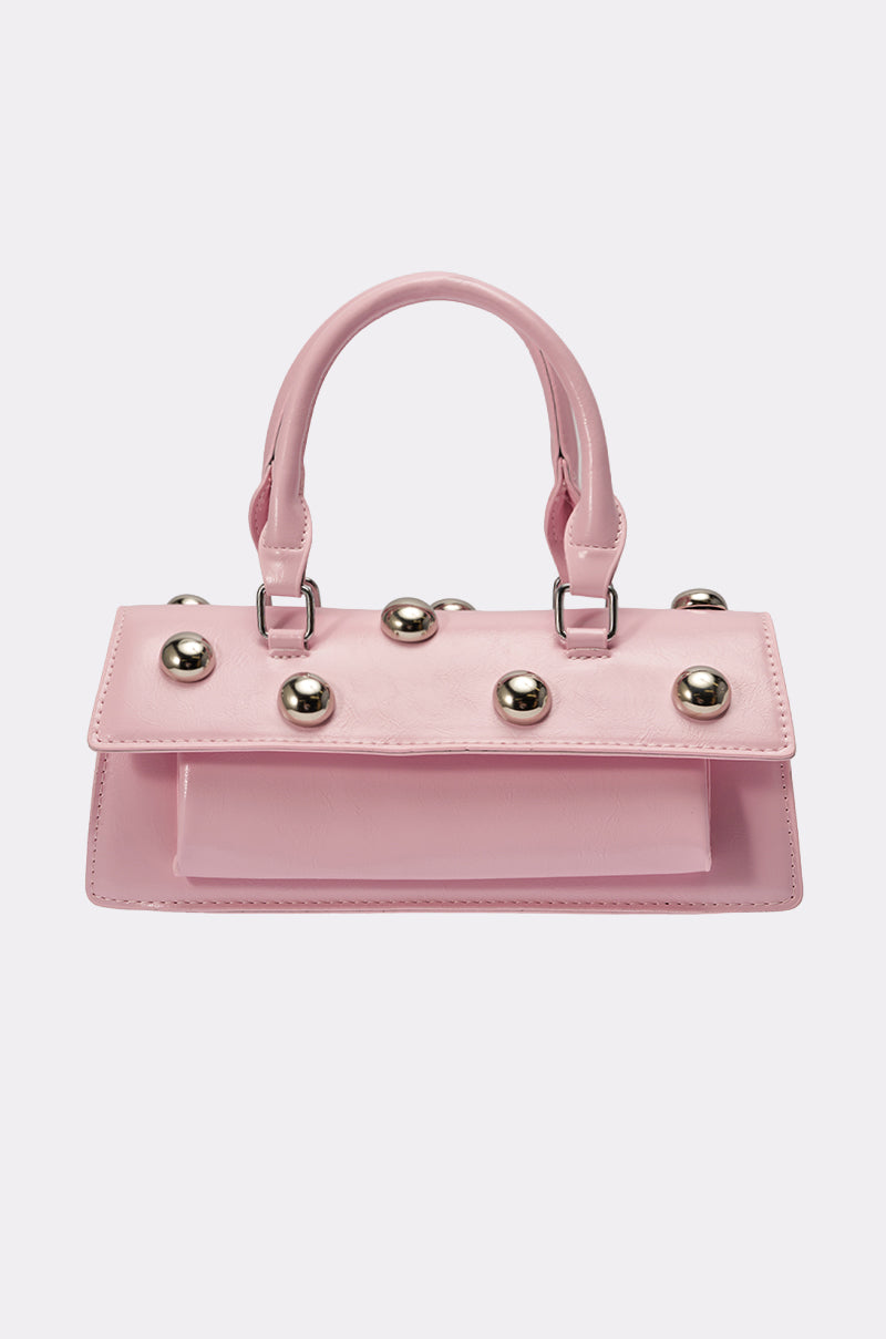 The PERRI DOME EMBELLISHED PURSE is a small, rectangular pink faux leather bag with a top handle, flap closure, evenly spaced silver studs, and sleek metallic hardware for a chic Y2K vibe. 1
