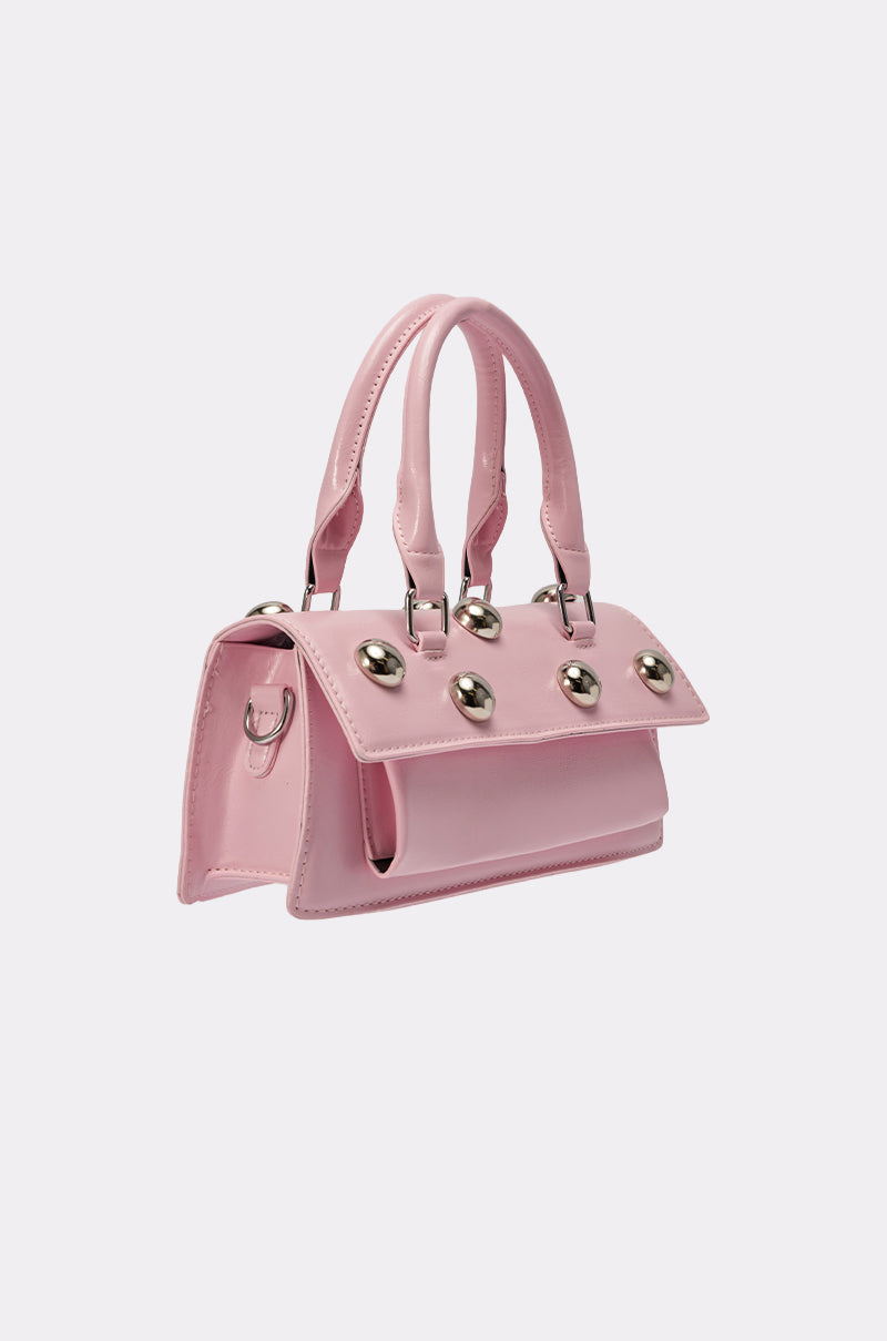 The PERRI DOME EMBELLISHED PURSE is a pastel pink faux leather handbag with double handles and silver studs on the flap, channeling a chic Y2K vibe against a plain light background. 3