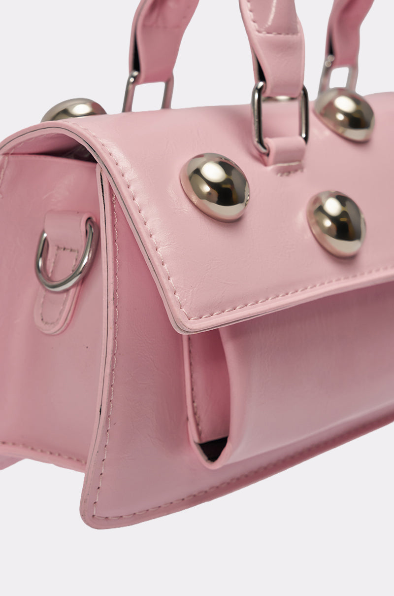 A close-up of the PERRI DOME EMBELLISHED PURSE, a pink faux leather handbag with silver dome studs, metal rings on the handle and side, a structured flap design, visible stitching, and bold Y2K-inspired style. 5