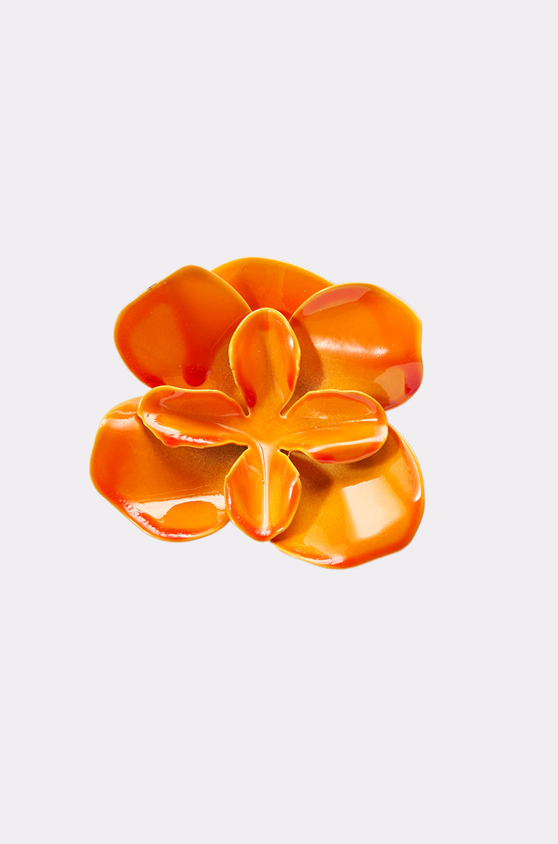 The ON DND EARRING is an orange, glossy, abstract flower-shaped accessory with five petals, resembling vibrant enamel earrings, shown against a plain light gray background. 5