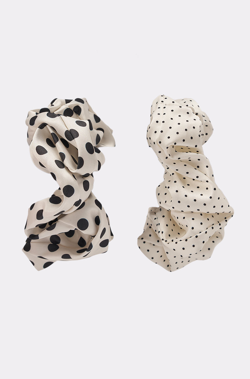The POLKA DOT IT SCRUNCHIE SET features two cream satin scrunchies with black polka dots—one with large spots, the other small—displayed side by side. These playful accessories add style to any hairstyle. 5