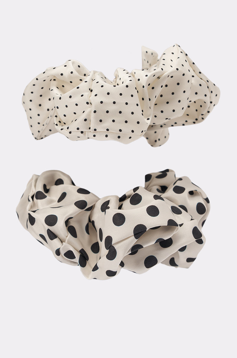 The POLKA DOT IT SCRUNCHIE SET features two beige fabric oversized scrunchies—one with small black polka dots and one with large black polka dots—making stylish hair accessories, shown on a plain light background. 7