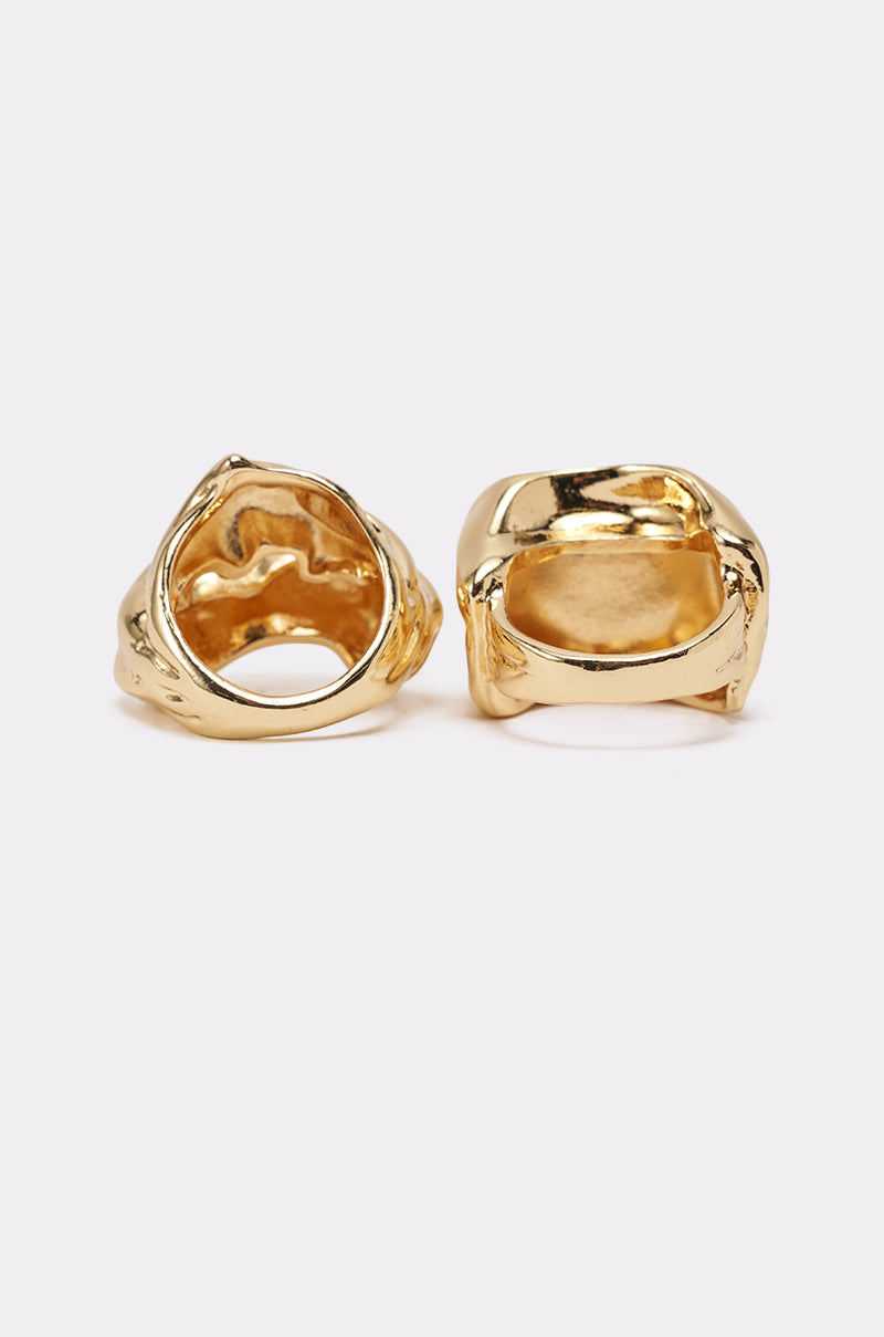 The MOLTEN DREAMS RING SET showcases two chunky gold rings with organic, abstract shapes and uneven surfaces, displayed side by side on a light background. Their hollow interiors highlight the sculptural design of this modern jewelry set. 3