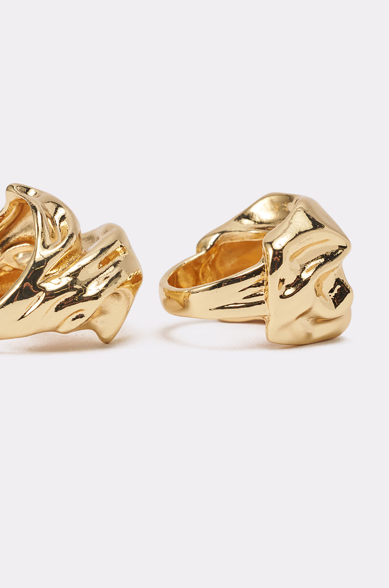 The MOLTEN DREAMS RING SET features two chunky gold rings with abstract, wavy forms, creating a bold sculptural look. Set against a light background, only parts of each modern piece are visible in the image. 4