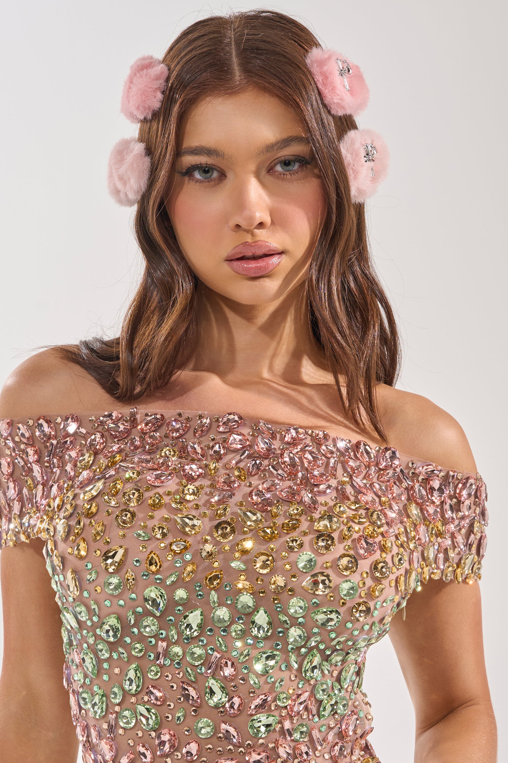 A woman with long brown hair wears GET IT FUR HAIR CLIPS as statement accessories and an off-shoulder dress with multicolored gemstones, looking directly at the camera against a plain background. 2