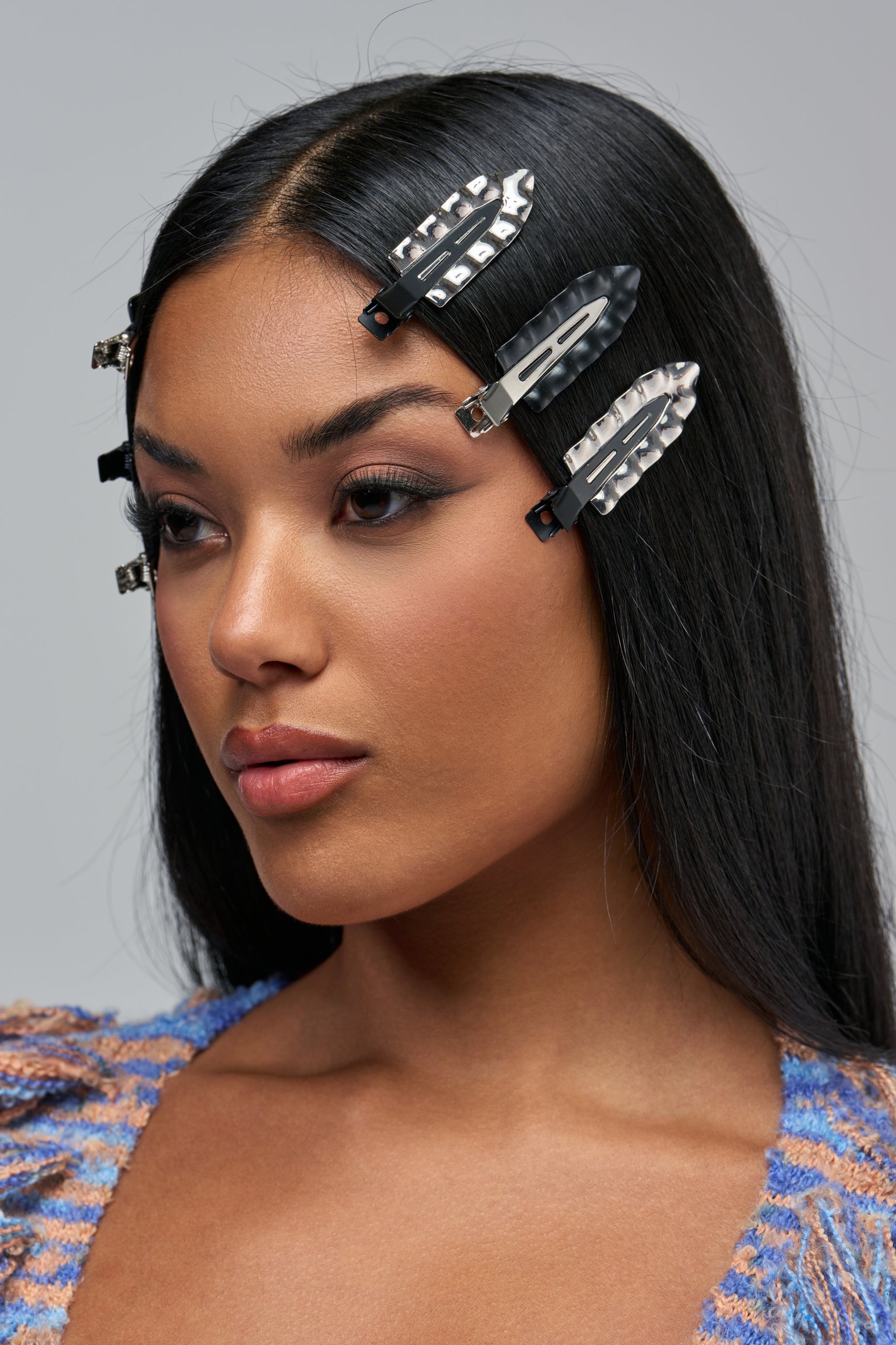 A woman with long dark hair wears HAIR CLIPS IN CHROME AND BLACK, a set of futuristic black and silver metal pins secured to the side.