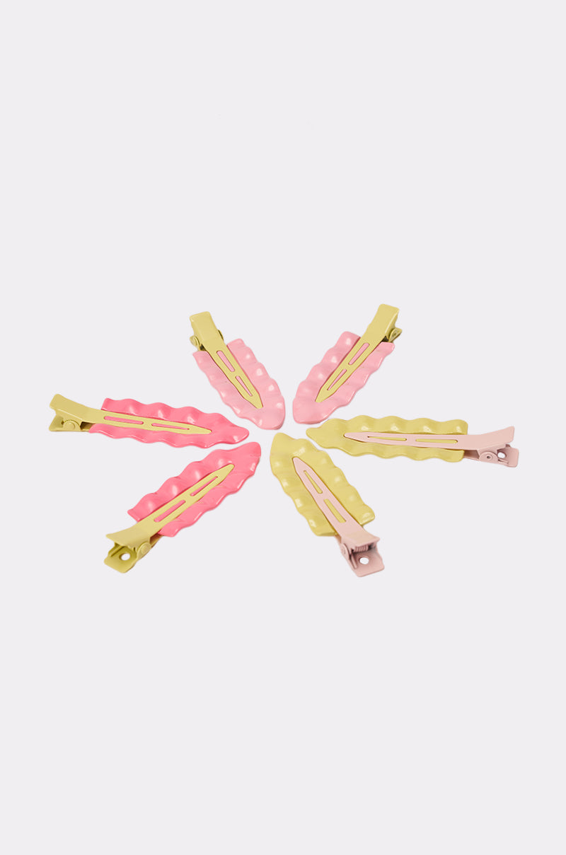 The PROUD OF U FLAT CLIP SET features six pastel enamel hair clips in pink, yellow, and beige with wavy edges and sturdy metal clasps, arranged in a circle on a white background for a playful retro look. 3