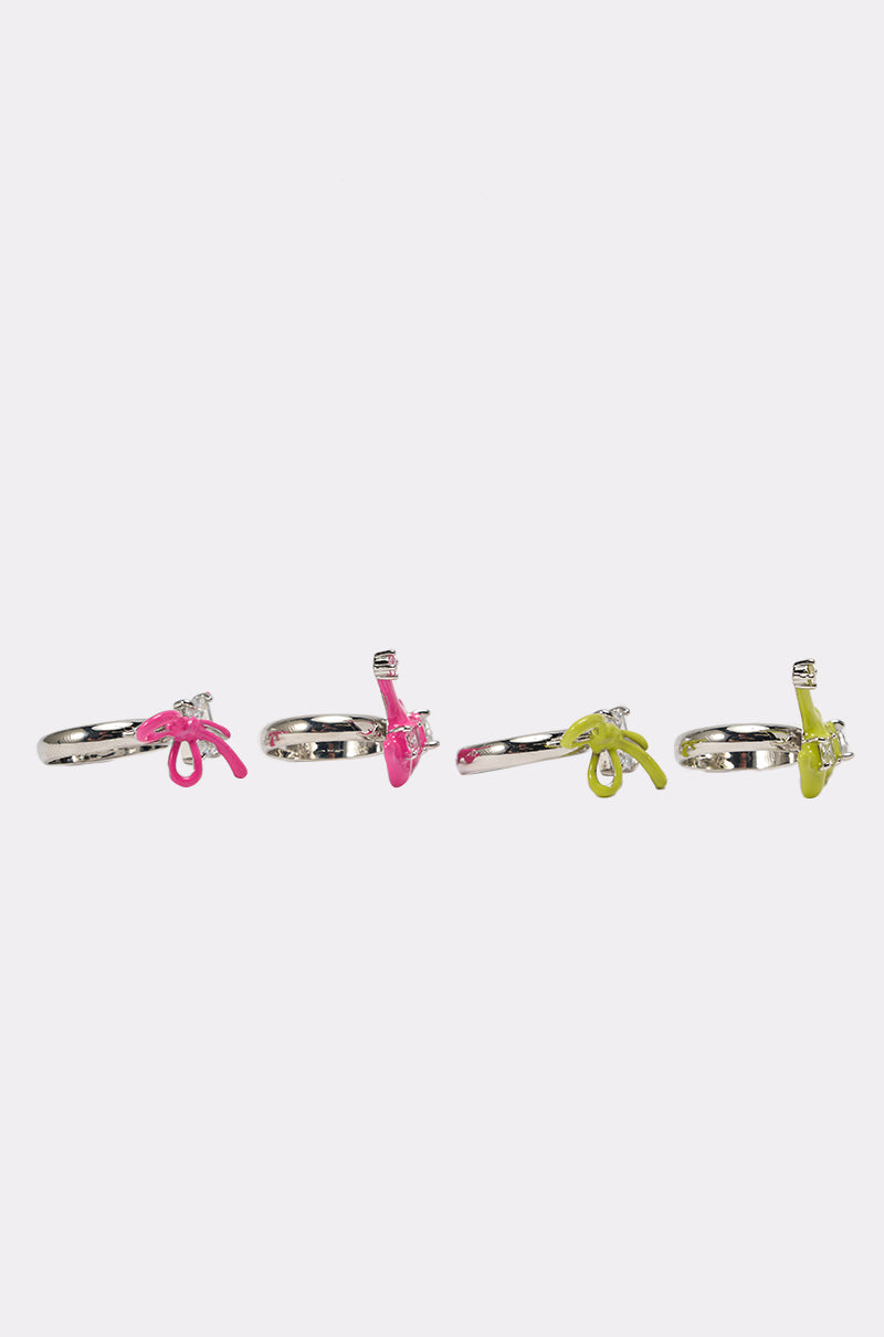 The TOO TRENDY RING SET includes four silver rings, each with a small plastic gun charm—two in bright pink and two in neon yellow—displayed in a row on a plain white background. 3