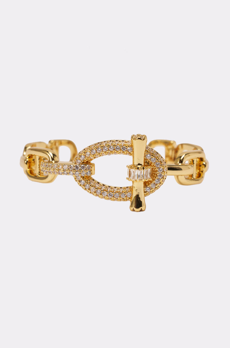 The IN THE LINK BRACELET is a gold statement cuff with an oval rhinestone centerpiece encrusted with small diamonds and a bar clasp, displayed on a plain white background. 1