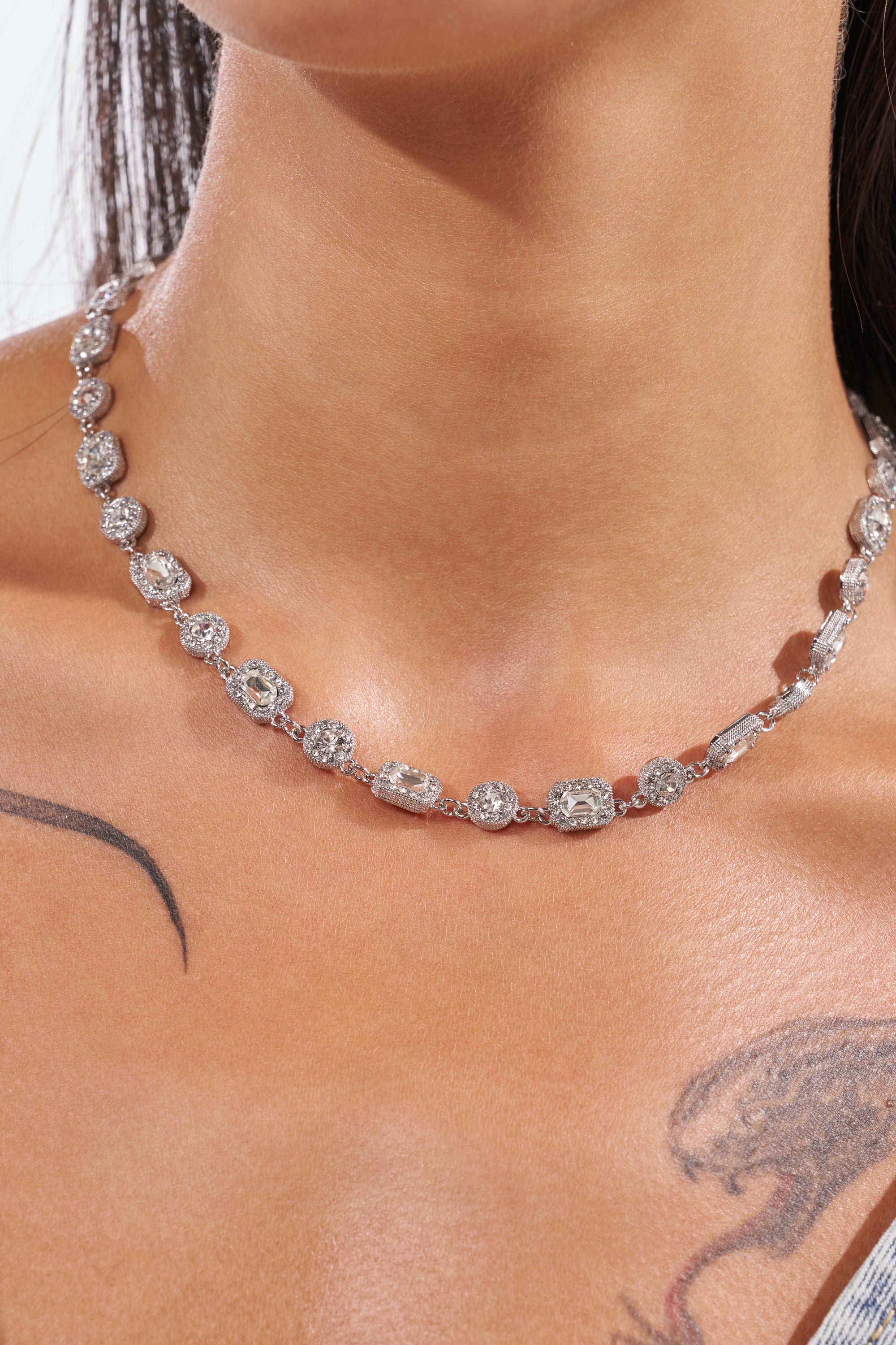 A close-up of someone wearing the REGAL CHAIN, a sparkling diamond formal necklace with oval and rectangular stones, highlighting their neck, shoulder, and chest tattoos—ideal for fans of glamorous jewelry. 1