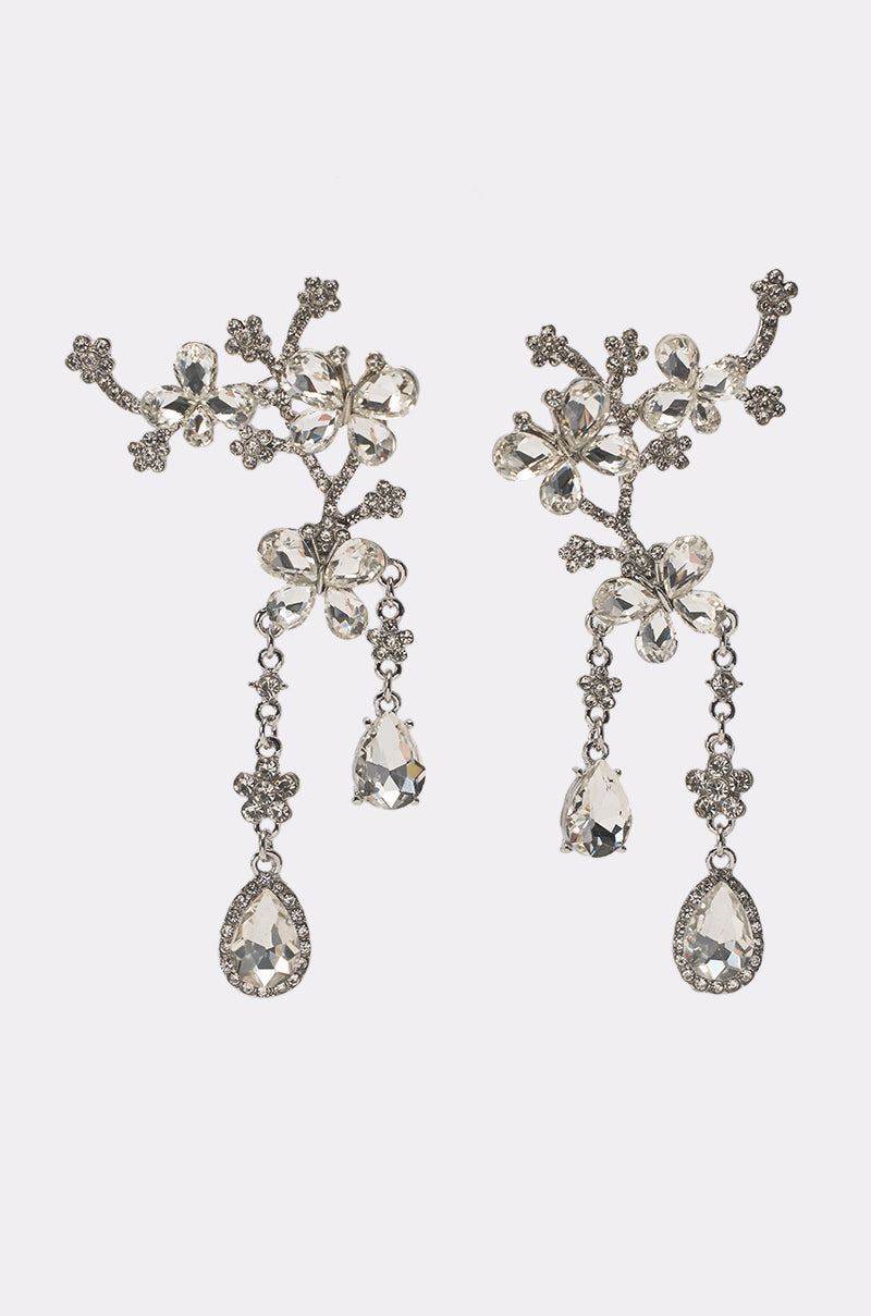 The WRAPPED AROUND EARRING is a pair of ornate silver wedding earrings with intricate floral designs, sparkling gemstones, and dangling teardrop-shaped crystals, shown against a plain white background. 1