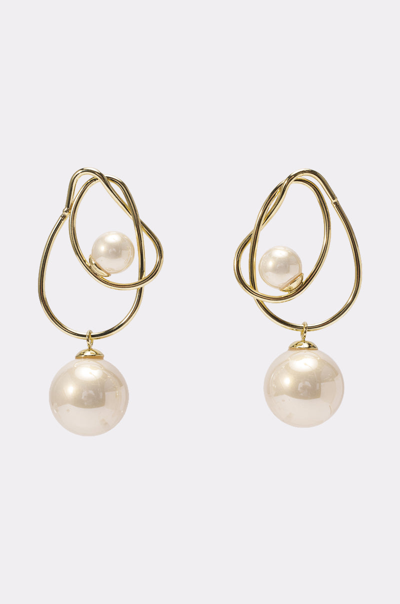 The DENNY EARRING features a gold sculptural, twisted design with a small pearl inside the loop and a larger pearl dangling below. Shown against a light-colored background, these earrings exude elegance and artistry. 0