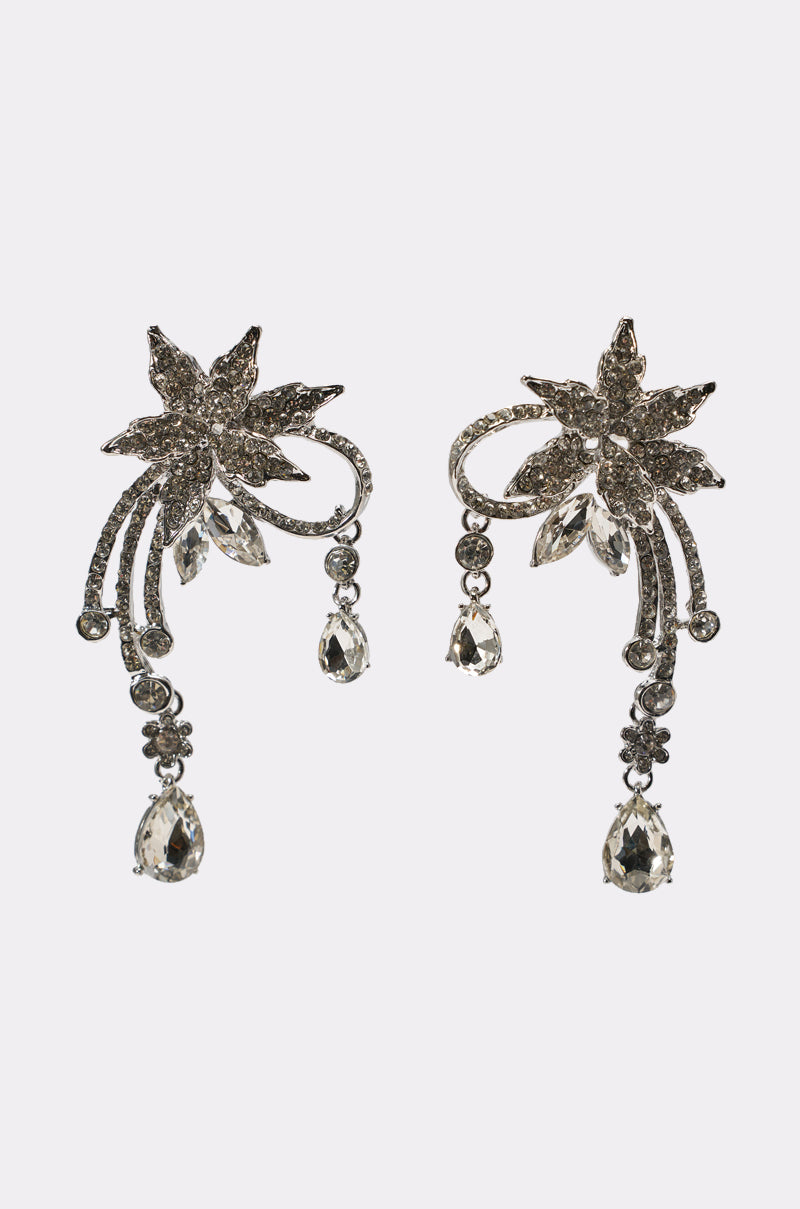 The TRIANA EARRING is an ornate pair of silver drop earrings shaped like flowers with leaf accents, sparkling crystals, and dangling teardrop gems—an elegant choice for bridal wear. 0