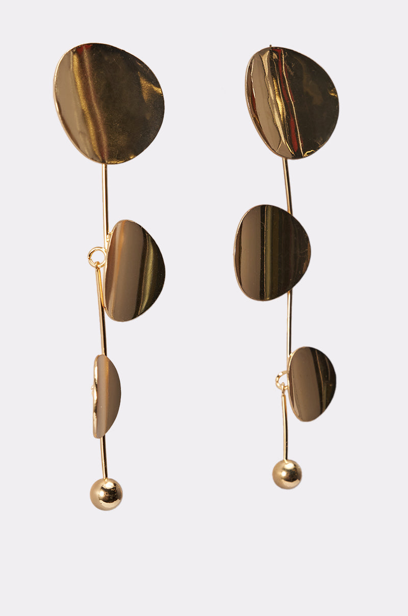 The DEDE EARRING showcases three irregular, flat gold circles connected vertically by a slender bar and accented with a small bead. These modern earrings feature an abstract design for a bold statement look. 2