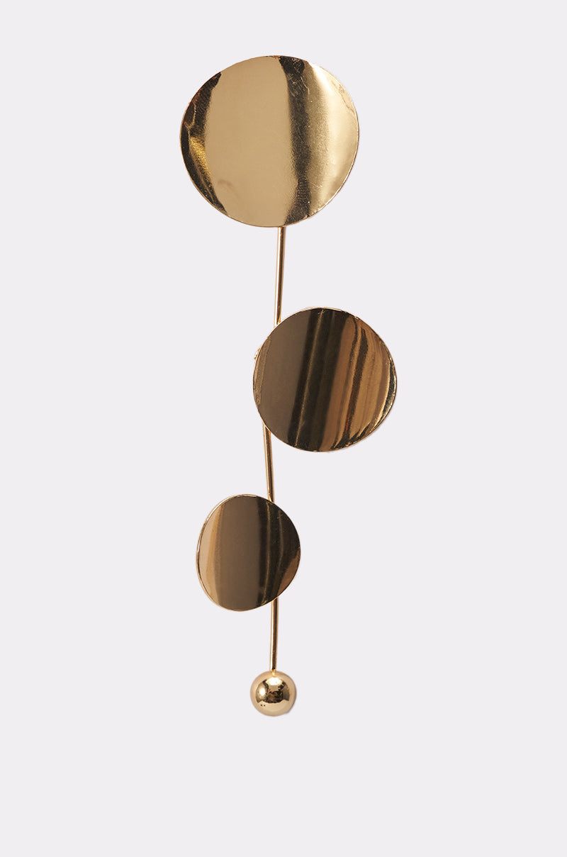 The DEDE EARRING is a minimalist gold accessory with three shiny, flat discs of varying sizes connected by a thin vertical rod and finished with a small round bead at the bottom, displayed against a light background. 3