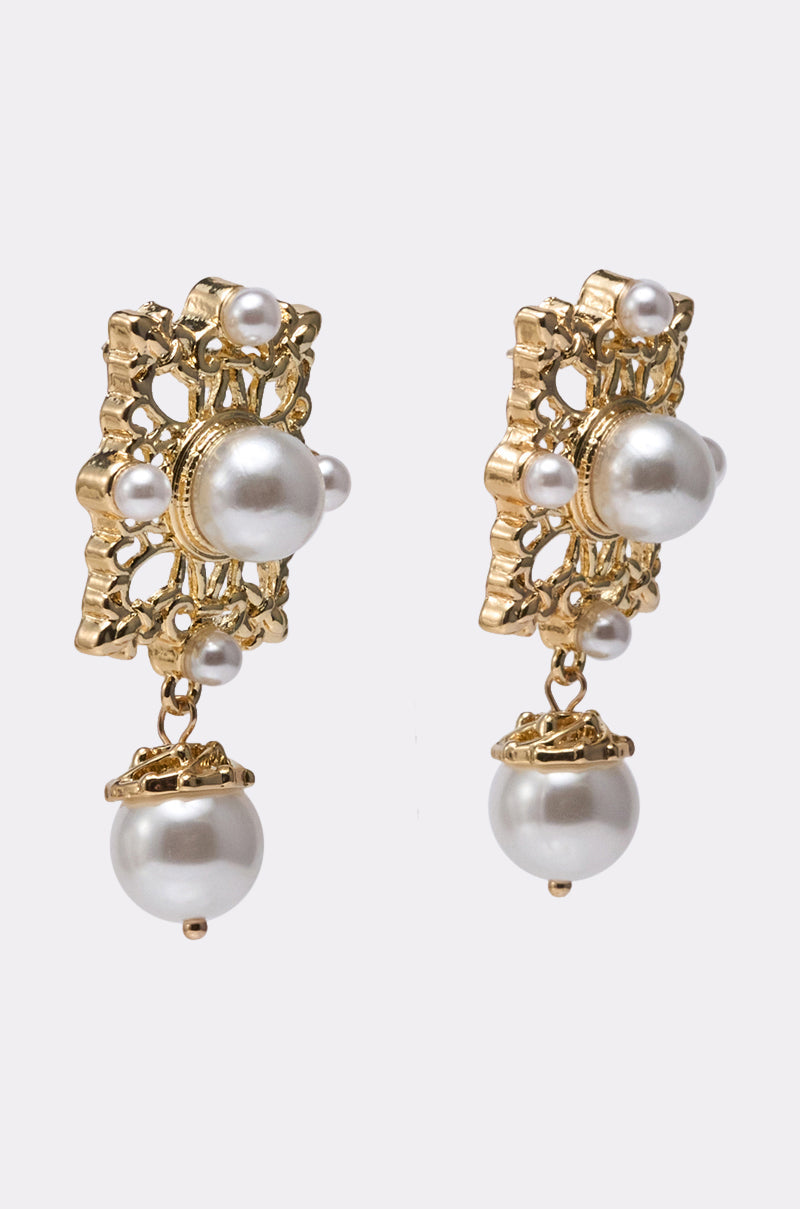 The REGENT VIBE EARRING features gold-tone dangles with a central white pearl and a larger pearl below, showcased against a plain light background. 1