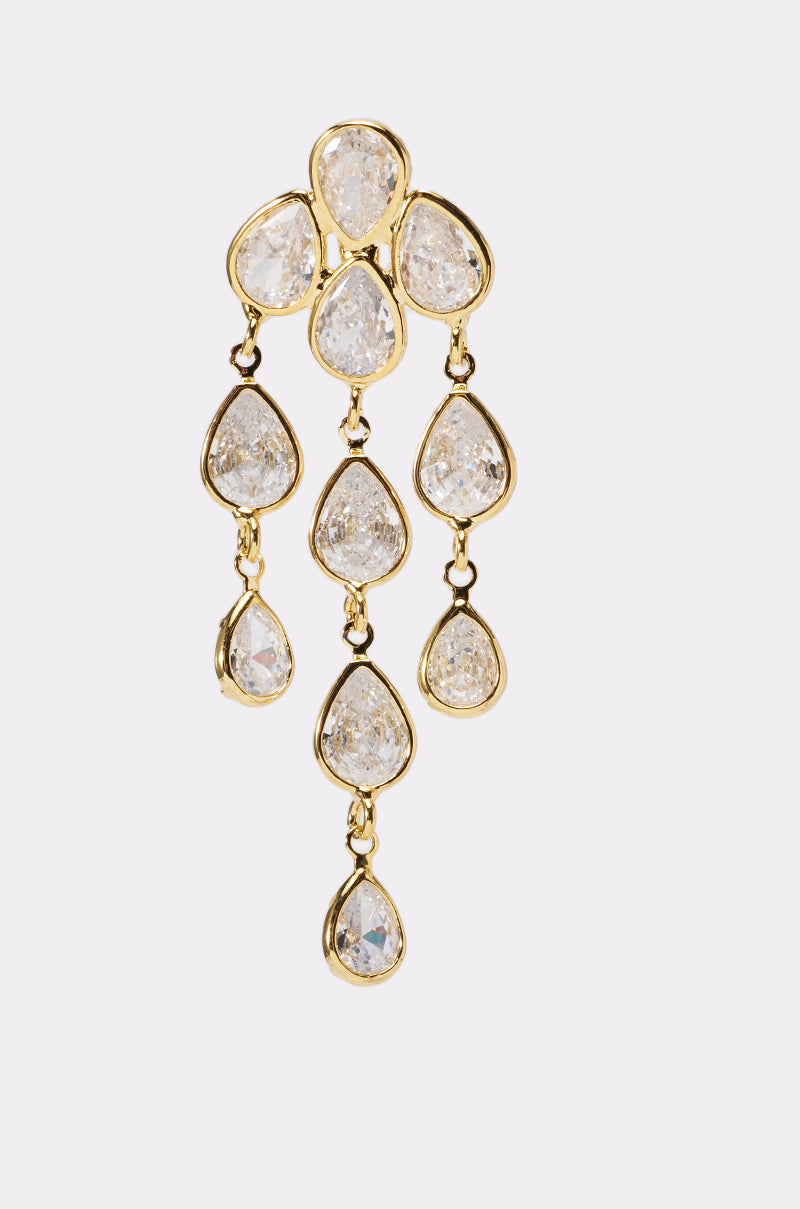 The LOVE ME EARRING is a gold chandelier-style piece with nine clear teardrop gemstones and three dangling sections, perfect as statement evening earrings against a light background. 2