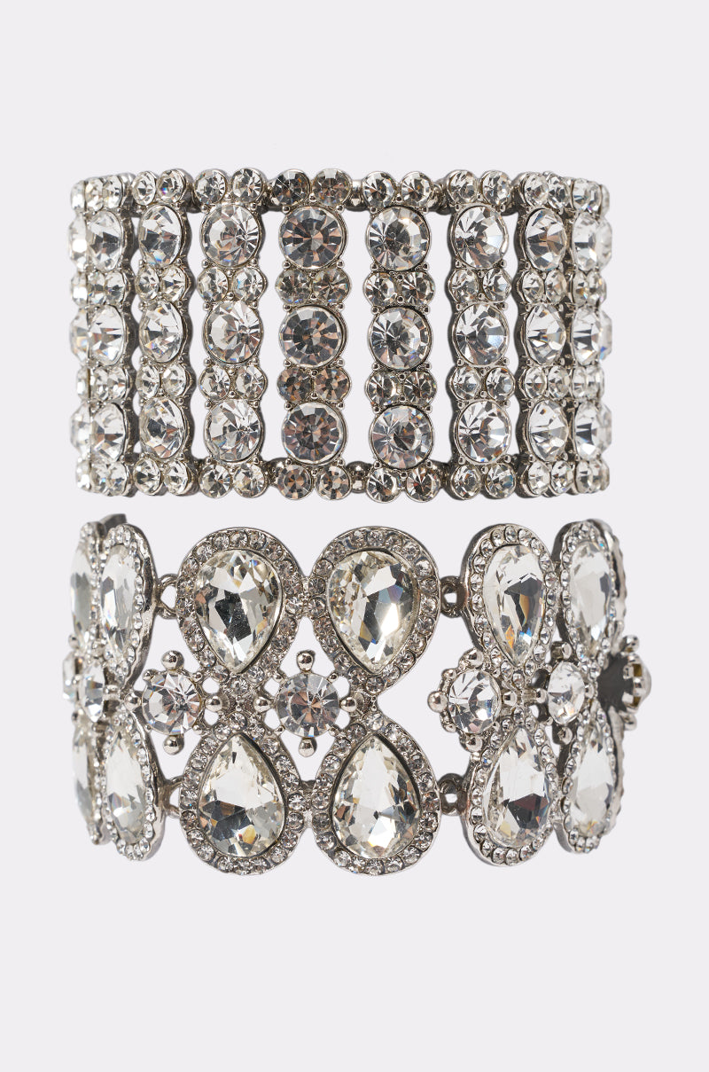 The ICE ME OUT BRACELET SET includes two silver cuff bracelets: one with vertical rows of round rhinestones, the other a stretch bracelet featuring teardrop rhinestones and floral details.