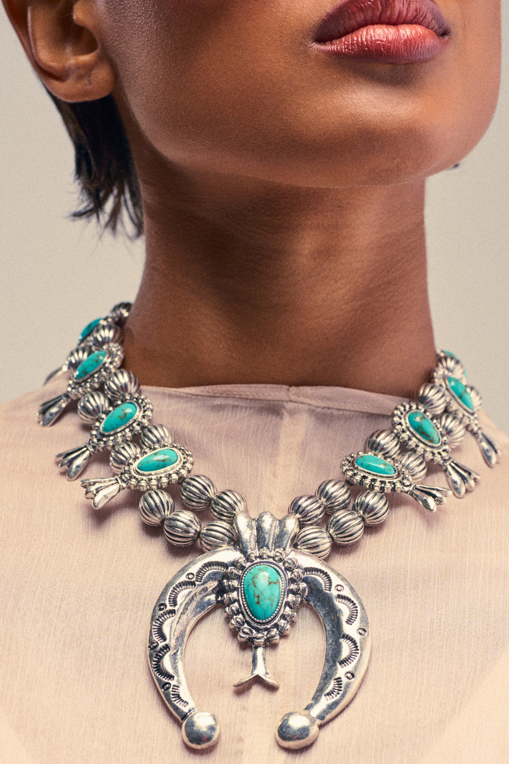 A close-up of a person wearing the I LIKE TO RIDE NECKLACE, featuring a vibrant turquoise gemstone and intricate silver detailing, paired effortlessly with a light-colored, sheer top—perfect for adding a touch of festival jewelry flair to any look.
