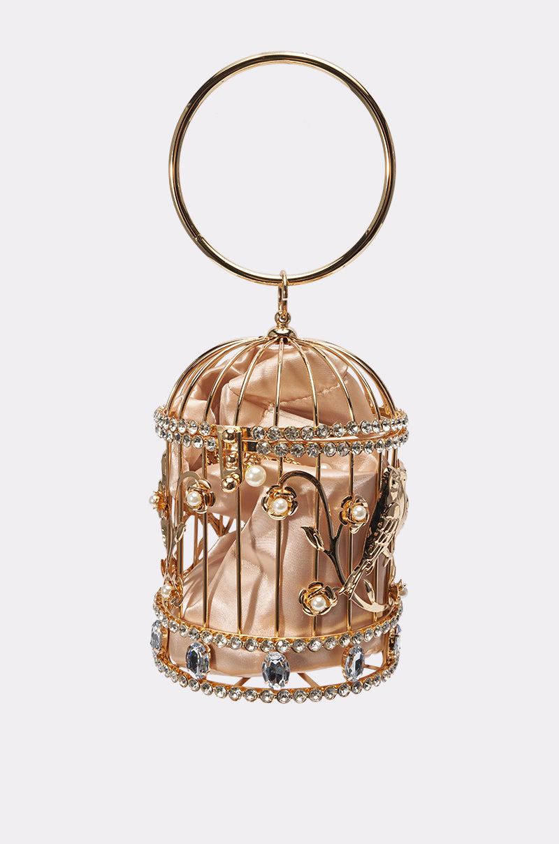 The NEVER CAGED LUXE BAG is a metallic gold, birdcage-shaped evening bag with crystals, floral accents, a circular top handle, and satin fabric interior.