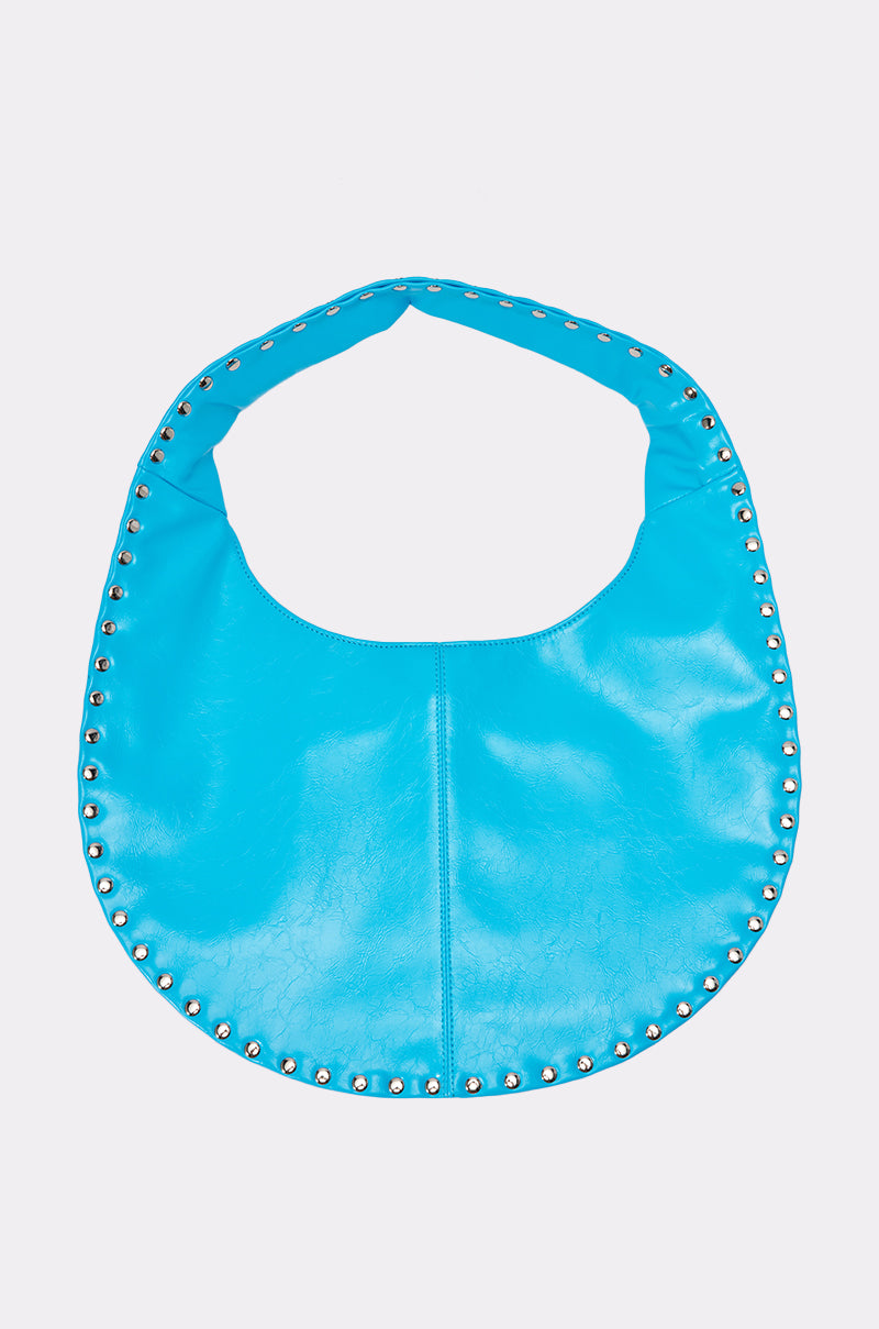 The COOL GURL STUDDED TOTE is a crescent-shaped blue faux leather bag with silver dome stud accents along the edges, shown on a plain light background.