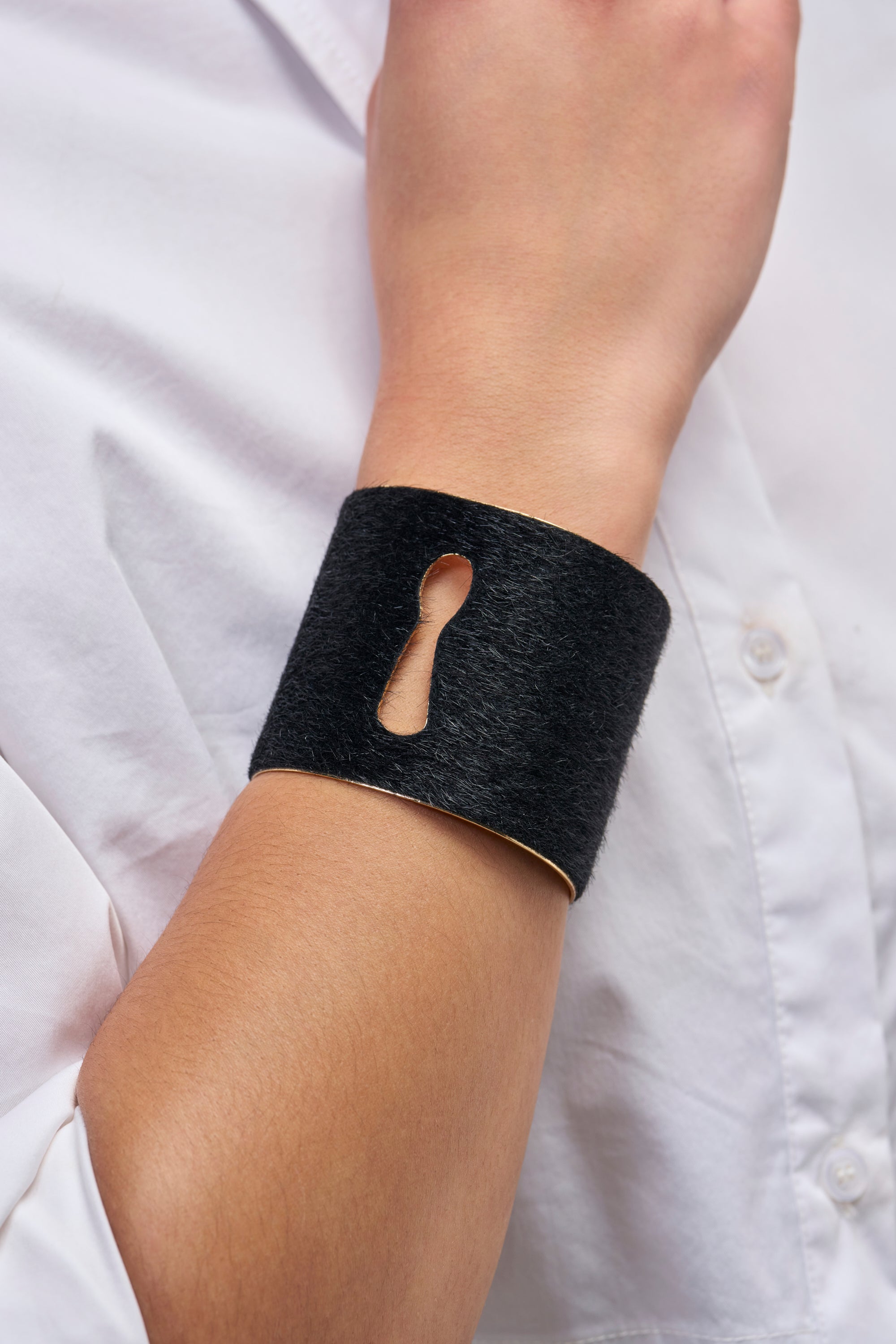 A black keyhole cuff bracelet from the MADE YOU LOOK METAL CUFF IN GOLD collection worn on a wrist.