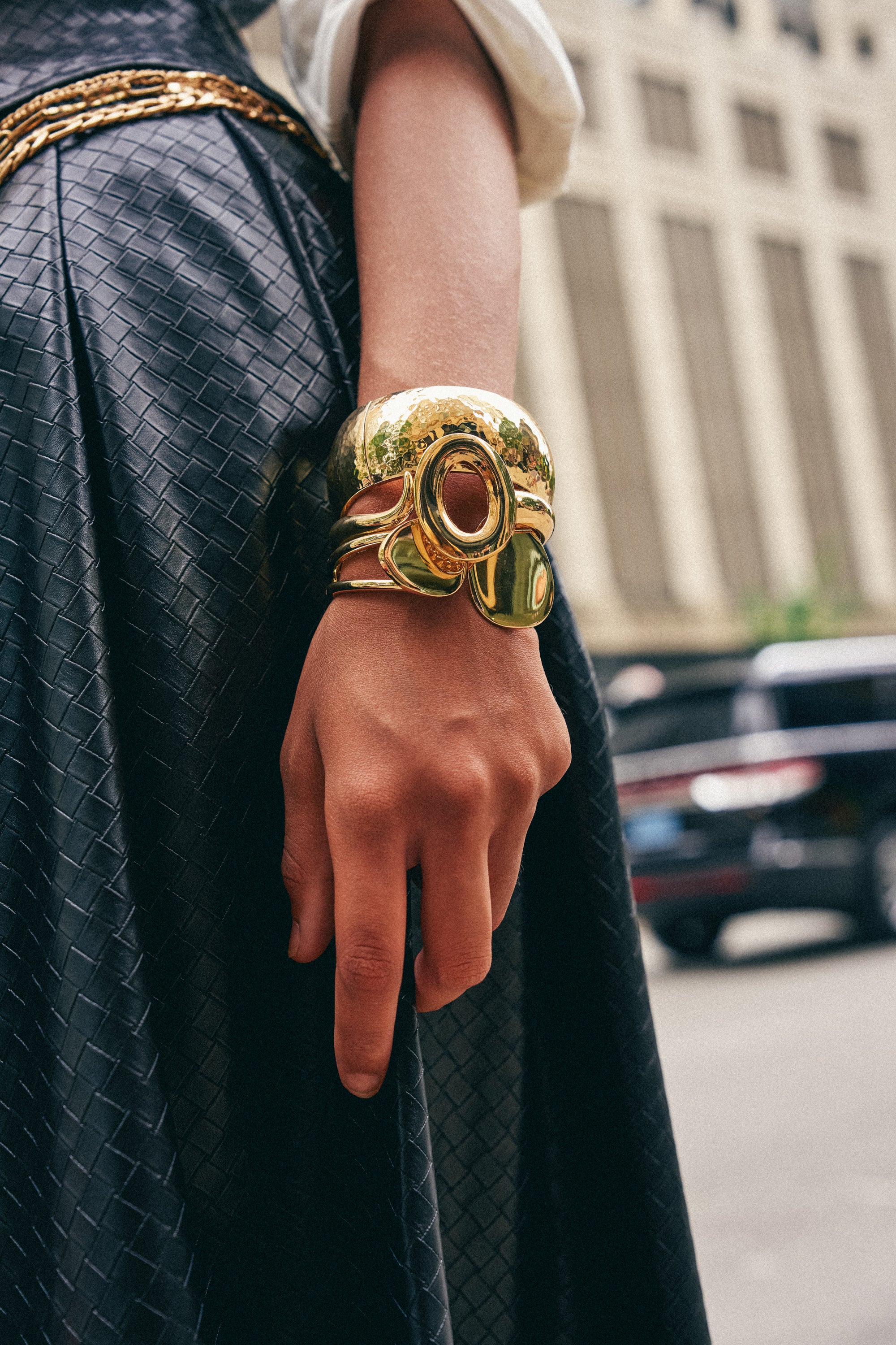 A person wearing a black textured dress stands outdoors with their hand relaxed by their side, showcasing the LIQUID GOLD BANGLE STACK.