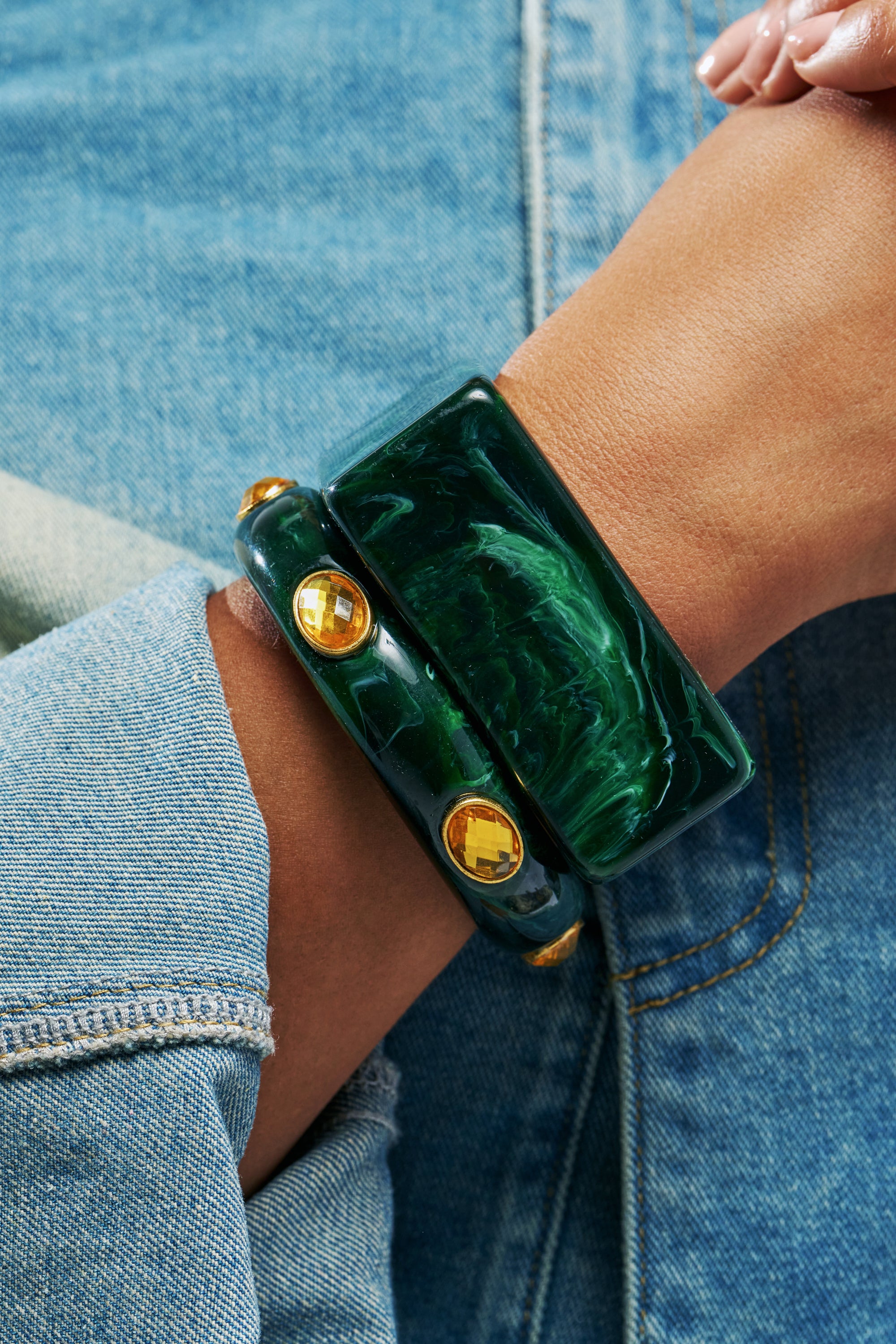 IT GIRL BANGLE SET IN GREEN featuring two emerald green resin bangles on a wrist, one wide and one slim with inset gold-tone gemstone accents.