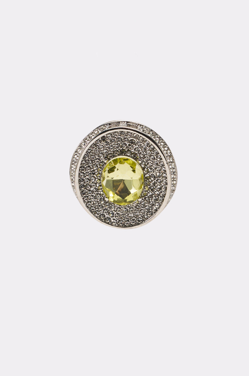 The RAY EARRING is a circular silver-tone accessory with a large faceted yellow gemstone at the center, accented by small rhinestones, displayed against a plain white background. 3