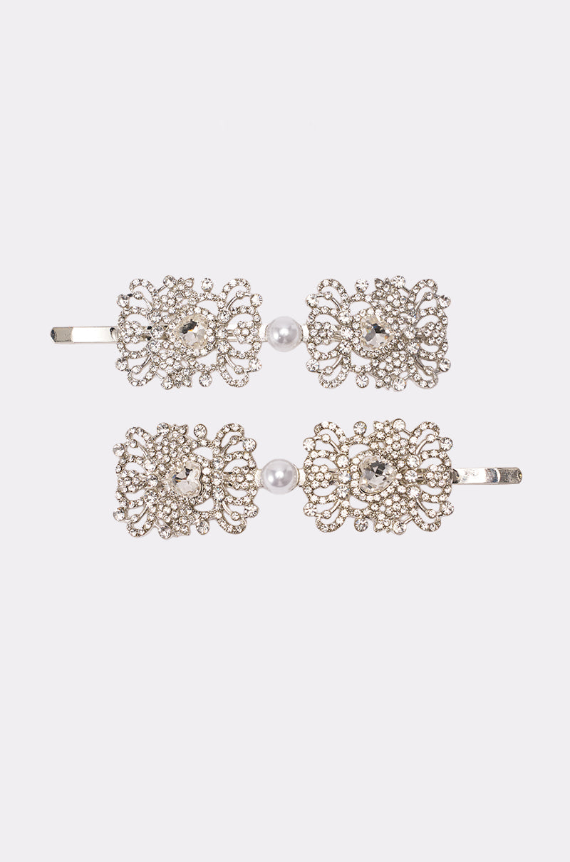 The REGENCY HAIR CLIP SET features two ornate silver hairpins with intricate filigree, rhinestone gems, and a single white pearl at the center, displayed on a plain white background. 2