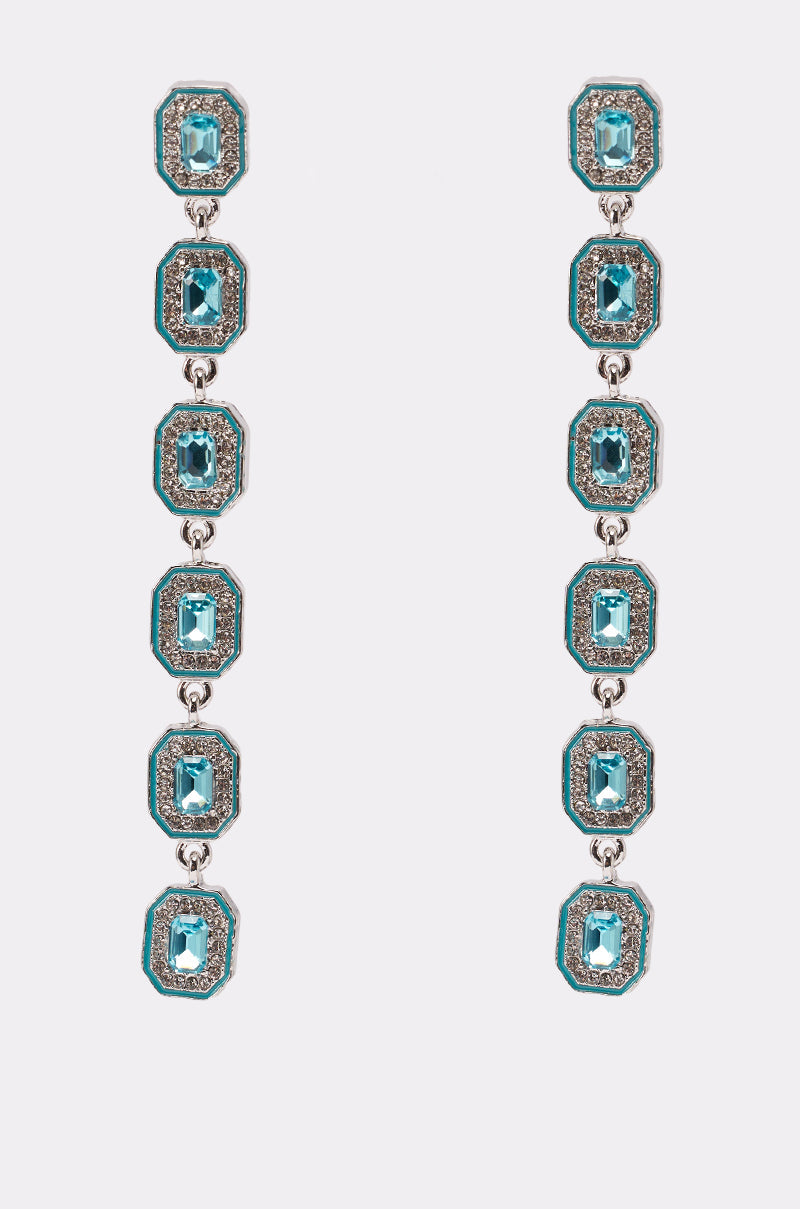 The TOO RICH EARRING is a pair of long statement drop earrings, each with five linked emerald-cut aqua blue stones bordered by sparkling rhinestones, shown on a white background. 0
