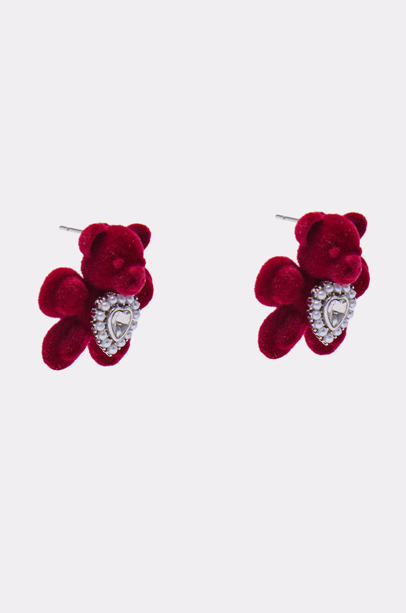 A pair of HUG ME EARRING red velvet teddy bear earrings featuring silver heart-shaped ornaments on their chests, displayed on a plain white background. 2