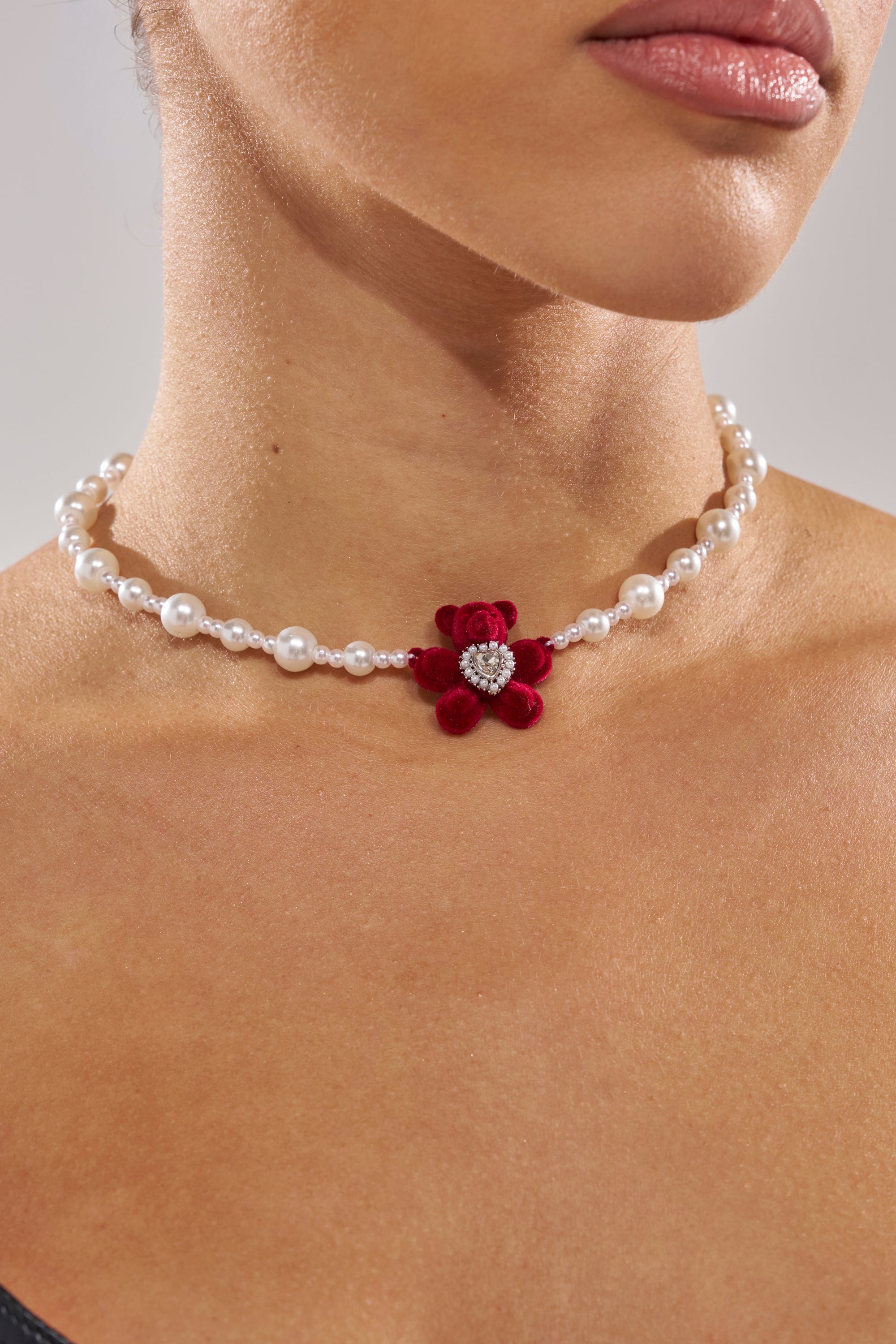 A woman wears the HUG ME NECKLACE, featuring pearls with a bear pendant and a heart-shaped centerpiece. The photo captures her neck and lower face, emphasizing the necklace’s playful yet elegant style.