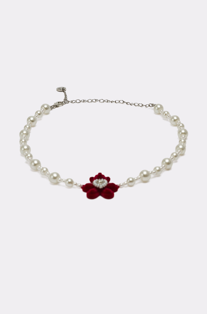 The HUG ME NECKLACE features a silver chain with pearls, a red velvet flower, central rhinestone detail, and an elegant heart gemstone, shown on a plain white background.