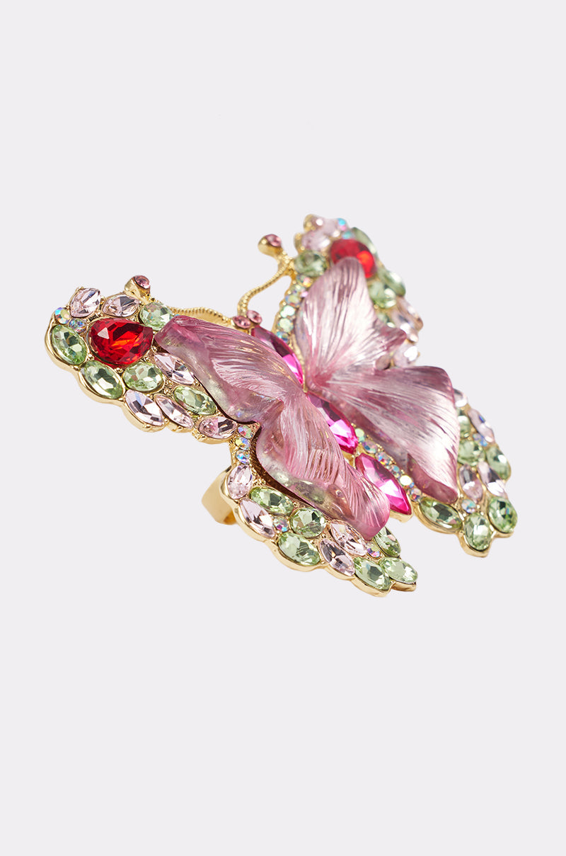 The SPREAD YOUR WINGS RING features a detailed butterfly with pink wings and gold edges, embellished with red, green, and light purple gemstones. Its ornate design stands out against a plain white background. 8
